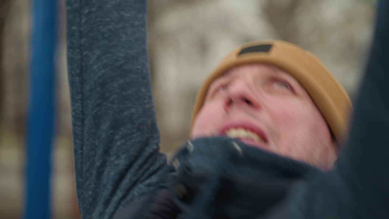 Close-up of a coach intensely working out, gripping a red iron bar as he pushes through and dropped down, with a blurred background