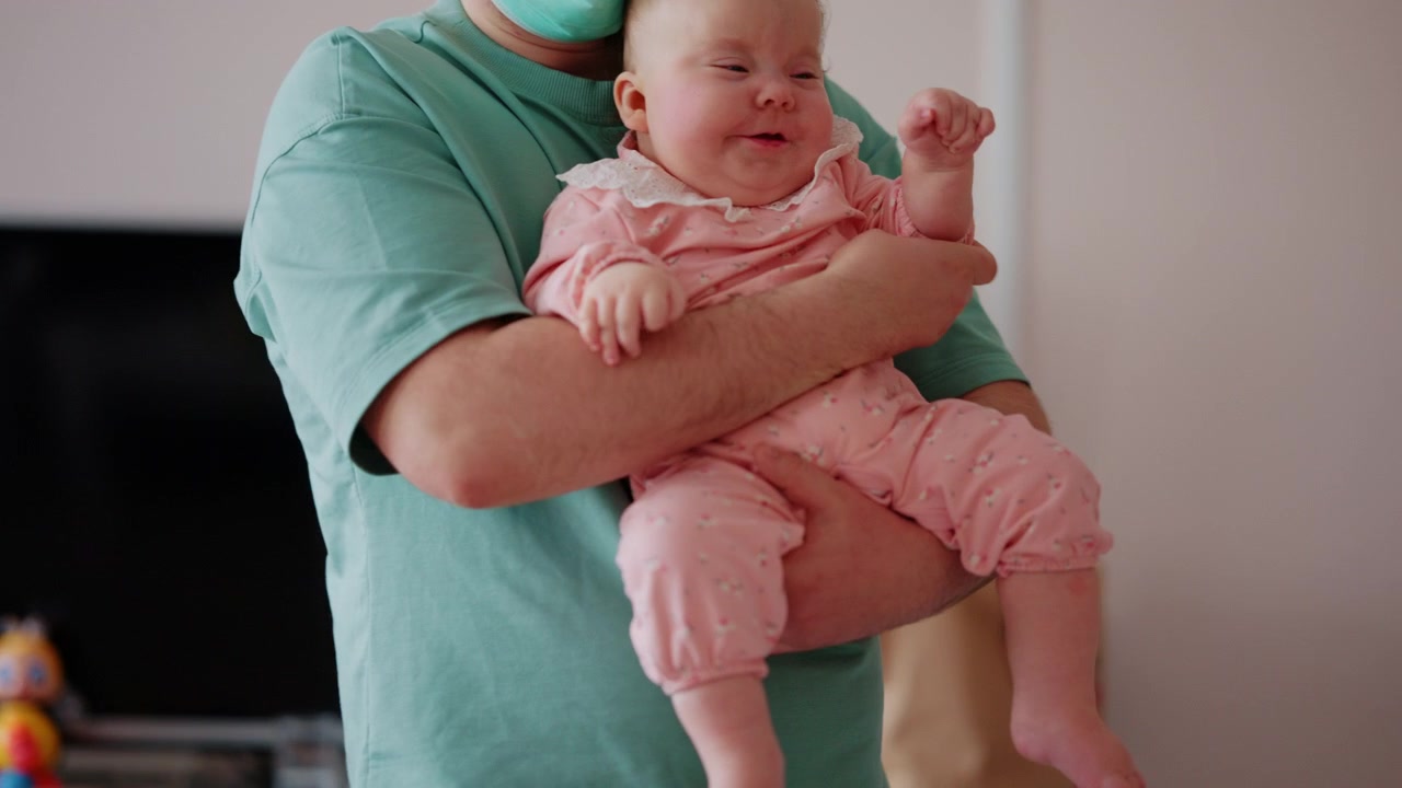 Profissional de saúde usando máscara médica, apoiando delicadamente um bebê durante uma sessão de cuidados pediátricos, com um brinquedo colorido por perto.