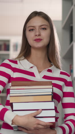 customer with book stack standing in store aisle. confident woman holds chosen literature for scientific essay in modern library. lady demonstrates folios