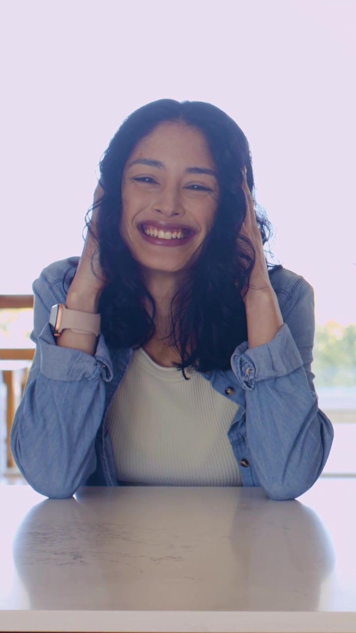 Video verticale: Donna in denim appoggiata che solleva i palmi al tavolo, girandosi a destra e parlando con l'orologio.