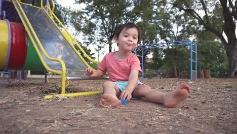 dolly in and out clip of an east asian boy kid having fun and smiling playing with toys sitting on the floor of an outdoor playground