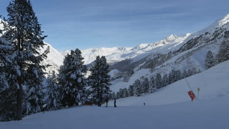 ski-piste-with-skiers-resting-and-mountains-in-background,-panning