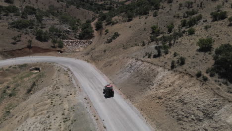 dron siguiendo a un camionero rojo conduciendo lentamente por una carretera en turquía karaman entre campos y montañas en un verano soleado aunque con curvas