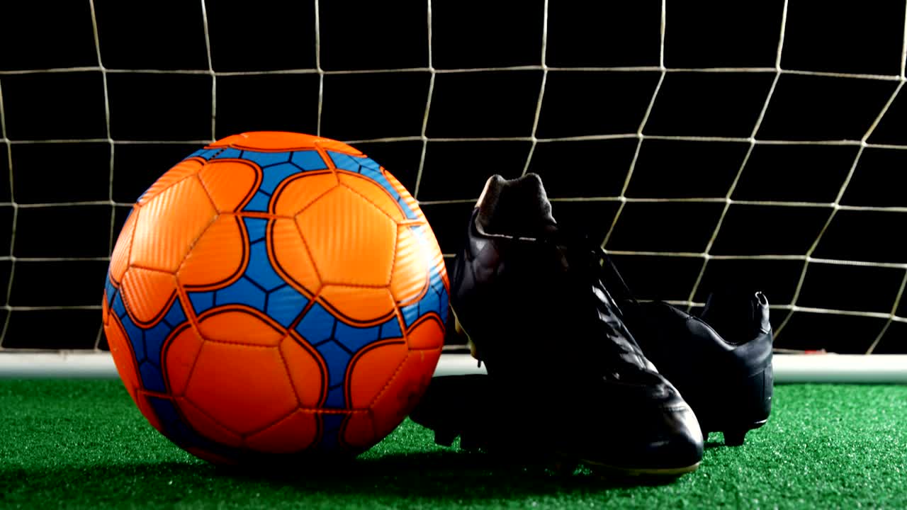 Primo piano di pallone da calcio e tacchetti su erba sintetica 4K