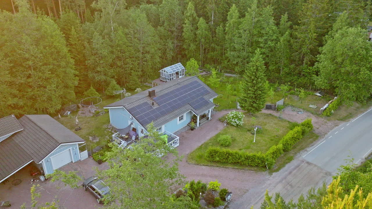 Kredsende luftfoto af et soldrevet økohus i den gyldne time midt i skoven.