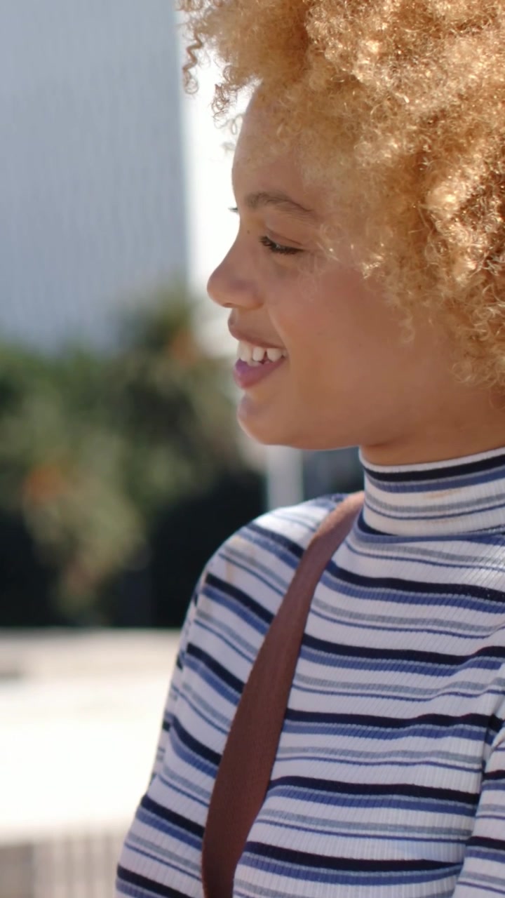 Vertical video: Glancing woman reading text and tapping phone on roof, striped tee and brown strap