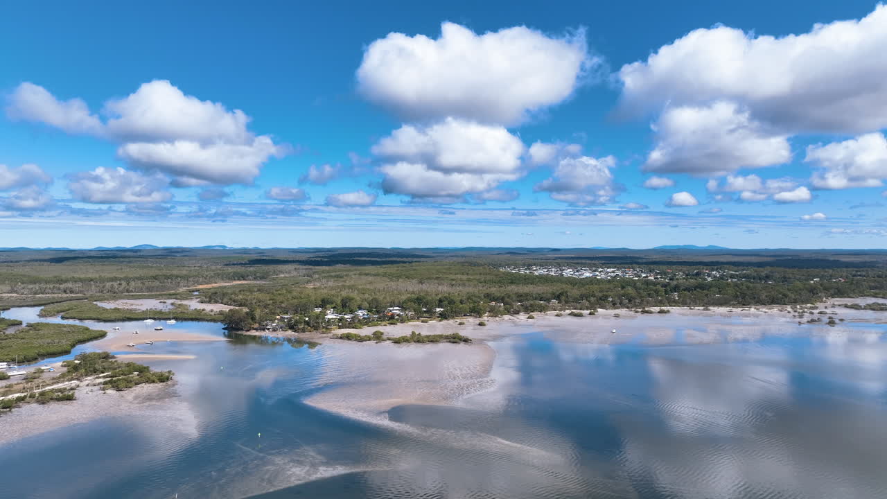 Flight over Tin Can Bay's reflecting waters towards village, forests, and inlet. Gorgeous calm summer's day