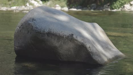 large boulder in a still river with dappled sunlight