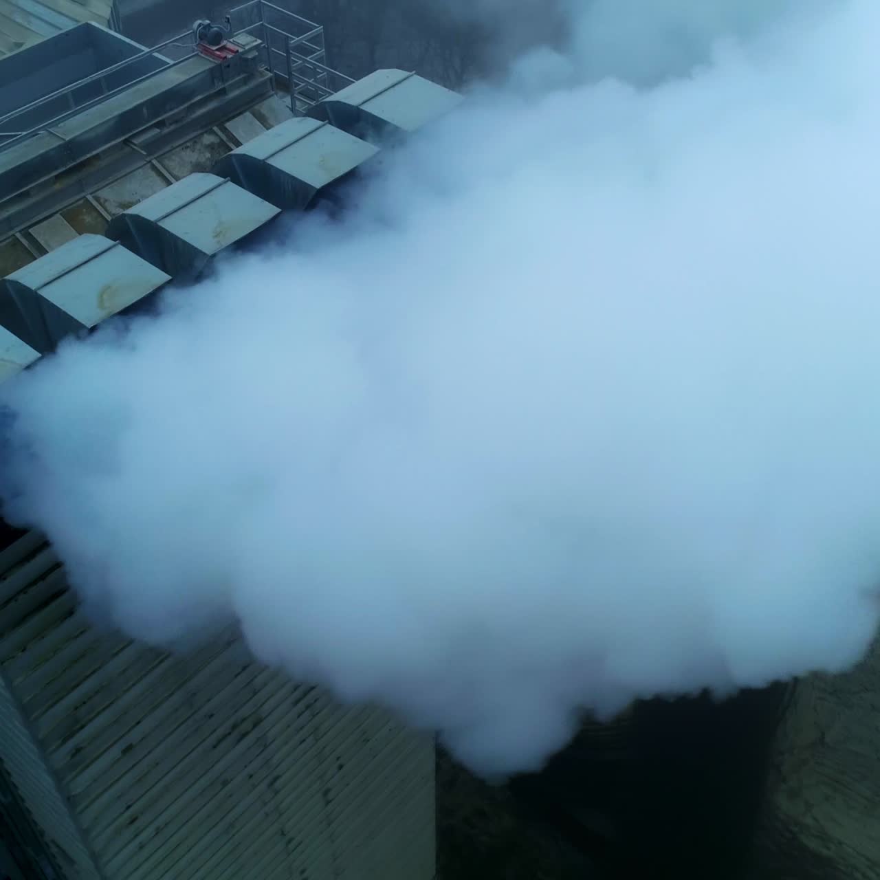 Working premises at elevator plant, thick pipes letting out heavy thick smoke. Flying above the tops of granary silo at the backdrop of grey weather
