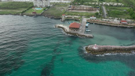 drone shot revealing with a small orbit the entire background around the wave breaker, the lighthouse, restaurant and the dock