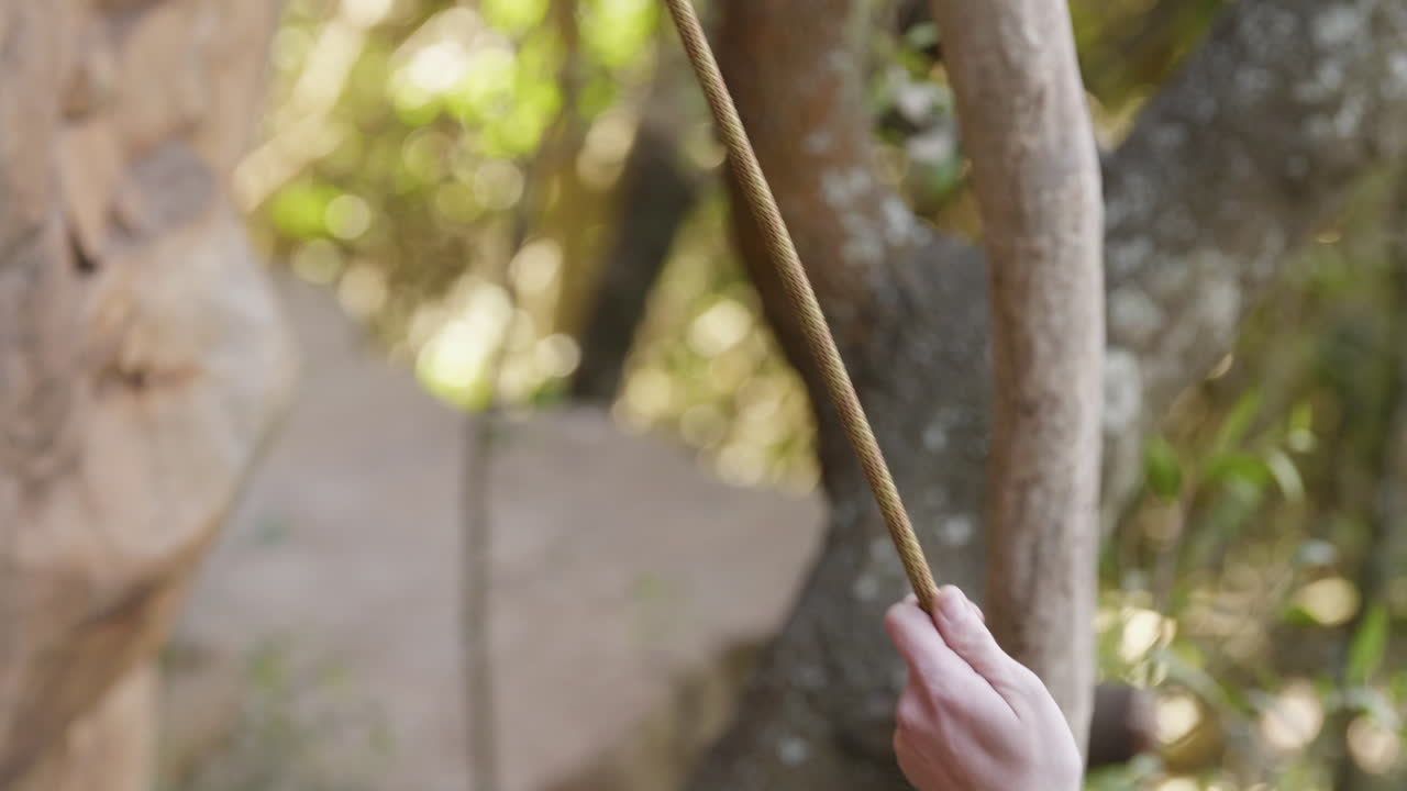 Close up of hand belaying rock climber rope with forest leaves in background