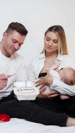 happy parents celebrating the second month of their first newborn child. smiling dad lights the candle on the festive cake. vertical video