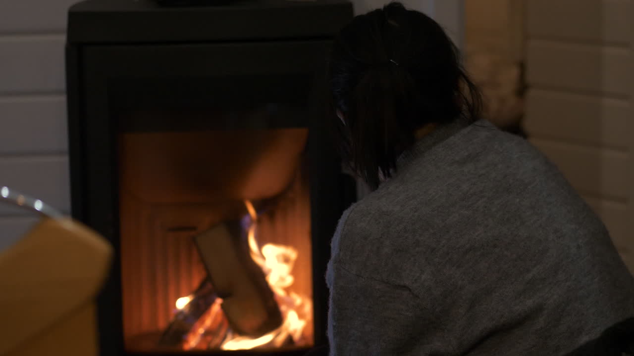 여자는 신중하게 실내 벽난로에서 통나무를 태우는 불꽃을 지켜본다