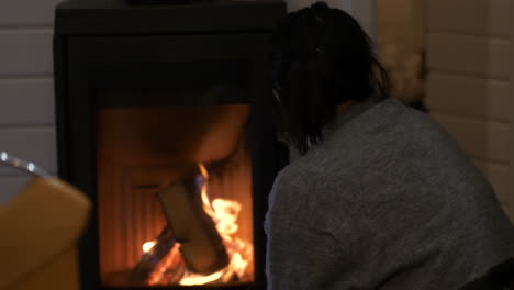 Woman-thoughtfully-watches-flames-burning-logs-in-indoor-fireplace