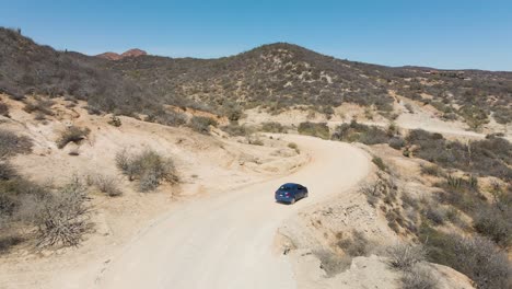 Antenne:-Kamerafahrt-Eines-Autos,-Das-Auf-Einer-Kurvenreichen-Schotterstraße-In-Der-Bergwüste-Fährt