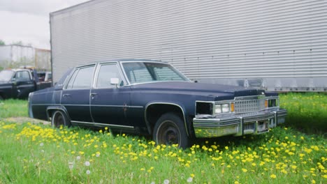 1970 년대 캐락 플리트우드 (cadillac fleetwood) 는 버려진 마당에서 녹는 트레일러 에 앉아 있습니다.