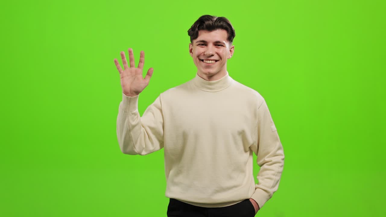 el hombre está de pie y mirando a la cámara. levanta la mano y saluda. se está riendo. está de pie sobre un fondo verde. pantalla verde. 4k.