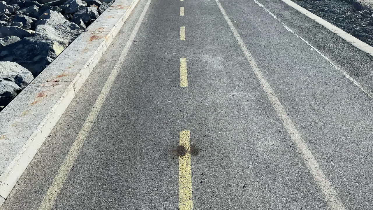 Um caminho se estende pela orla, com rochas de um lado e pavimento do outro, em plena luz do dia.
