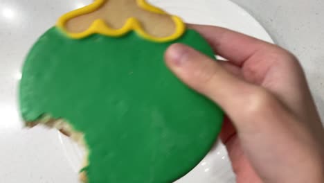 child taking a bite out of a colorfully decorated holiday cookie shaped into a christmas ornament