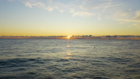 Low-Aerial-Shot-as-the-sun-peaks-through-distant-clouds-during-the-early-morning-sunrise-over-Lake-Michigan