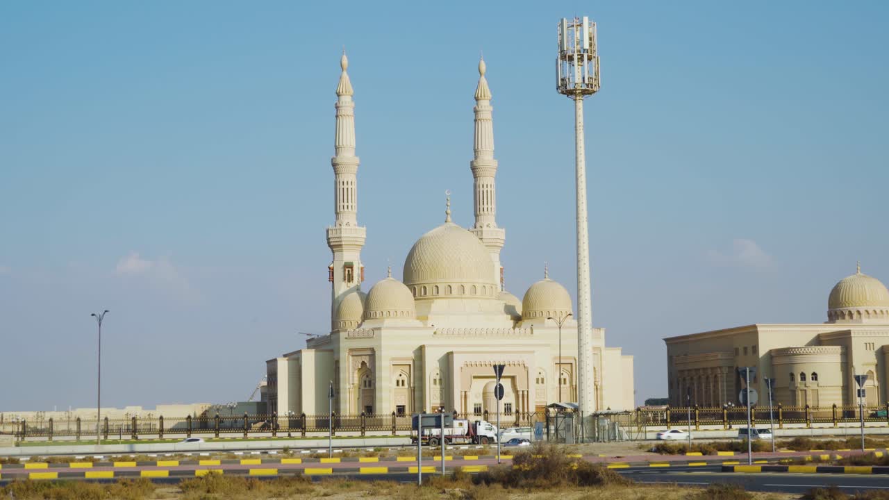 Veicoli sulla strada che passano accanto alla Moschea dell'Università Al Qasimia a Sharjah, EAU, in una giornata di sole - ripresa ampia