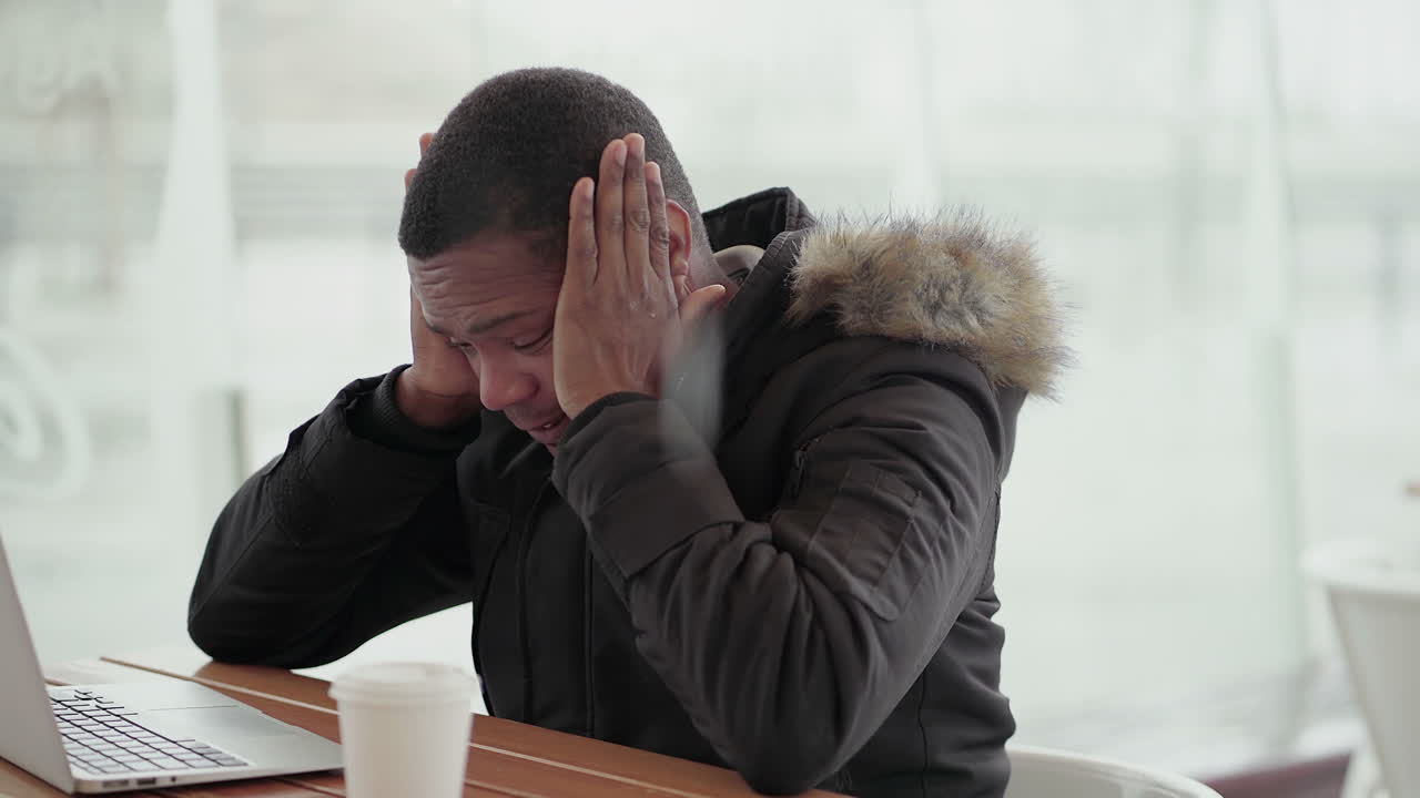 hombre afroamericano de mediana edad con chaqueta negra y capucha de piel trabajando en una computadora portátil afuera