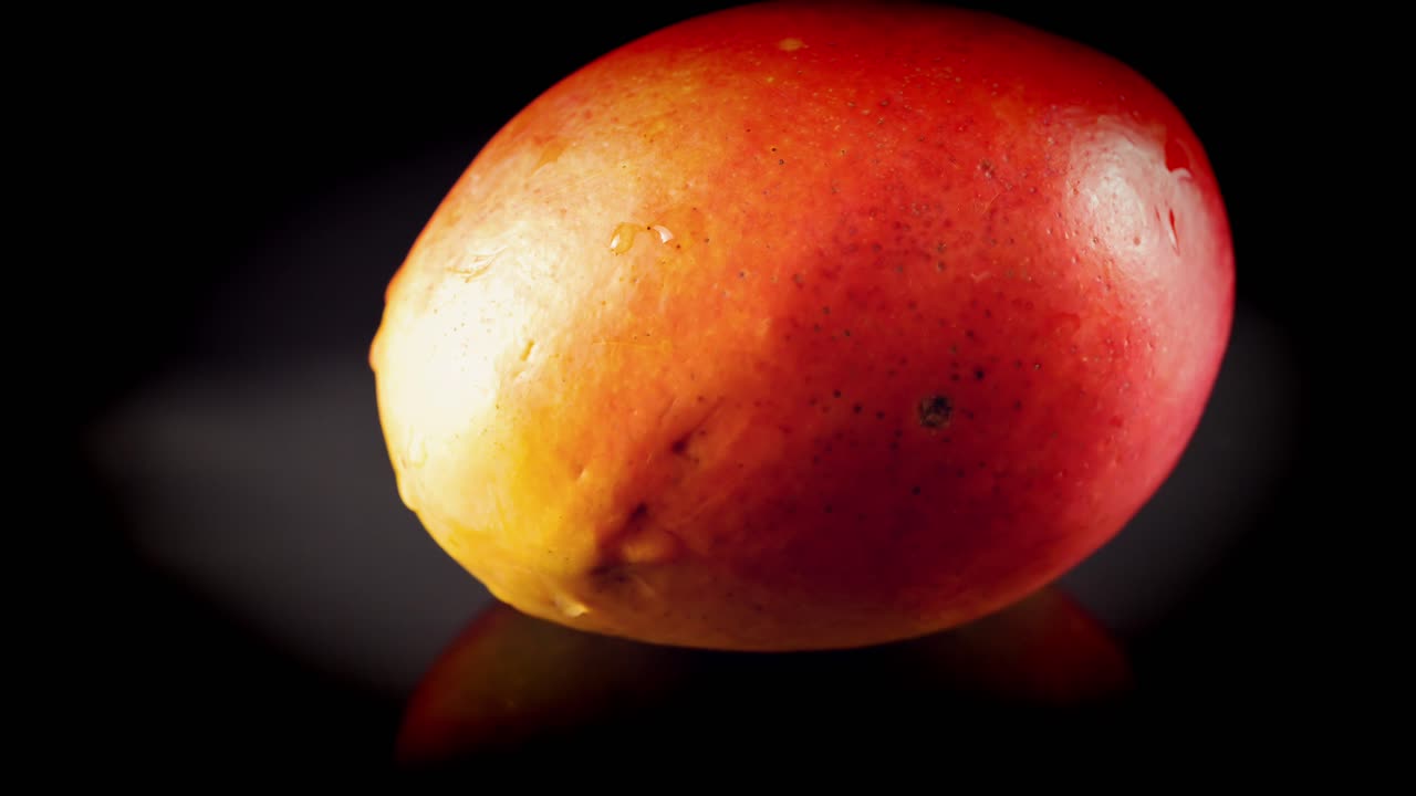 mango jugoso húmedo con deliciosas gotas de agua en la piel roja jugosa gira en cámara lenta sobre fondo negro