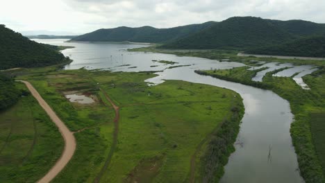 Aerial-footage-revealing-grasslands,-river,-rural-road,-gorgeous-lake-and-horizon-with-trucks-parked-as-people-come-for-camping,-fishing,-enjoying-the-outdoor-adventure