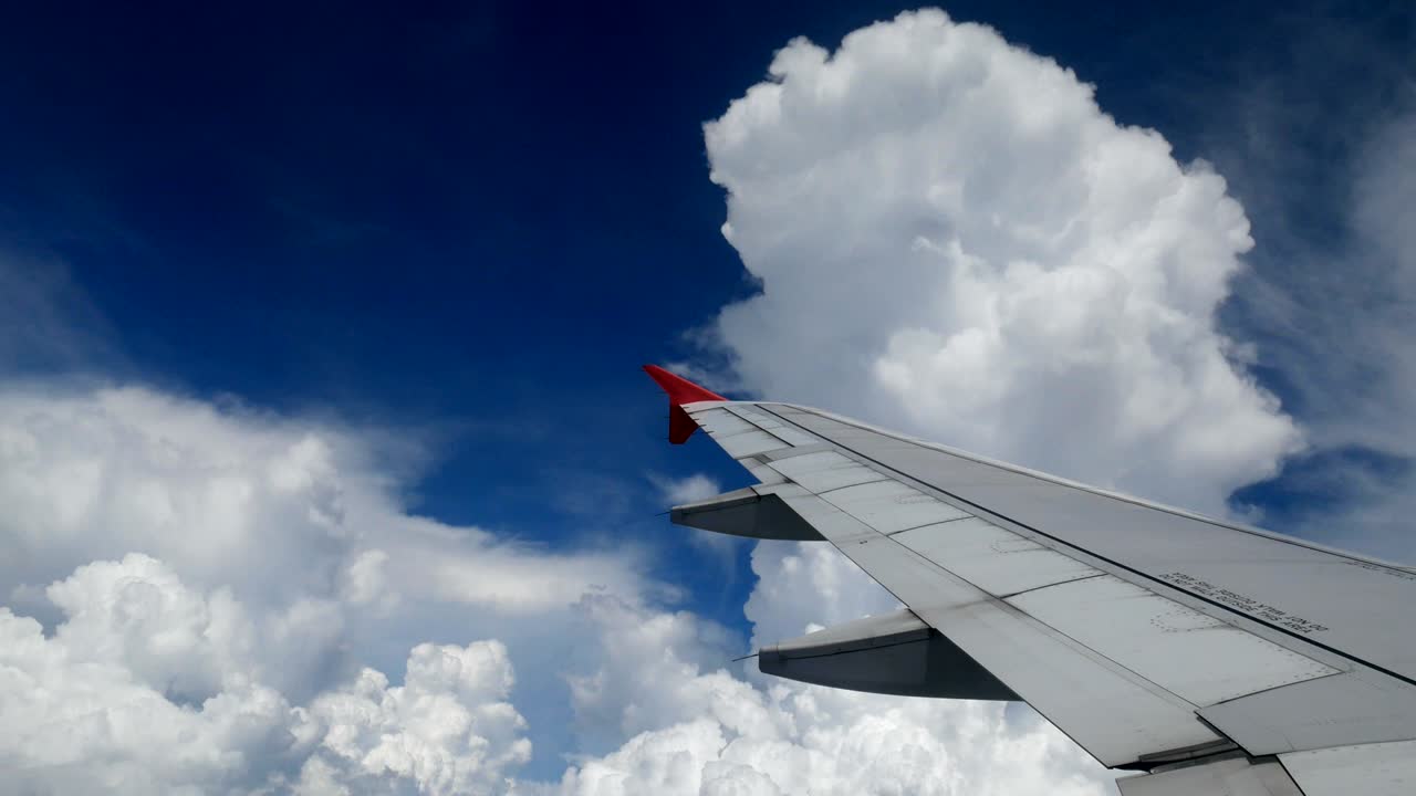 Metraje 4K. Viaje en avión. Vista aérea a través de la ventana de un avión. Ala de avión durante el giro para la dirección de aterrizaje y hermosas nubes blancas en el cielo azul para fondo de viaje.