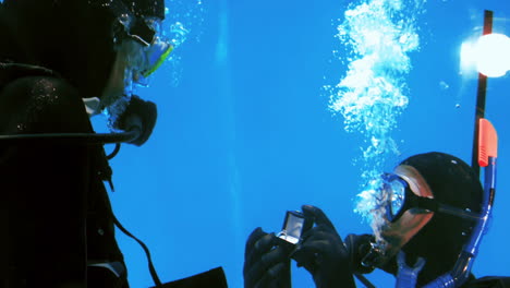 man in scuba diving offering engagement ring to woman in scuba diving