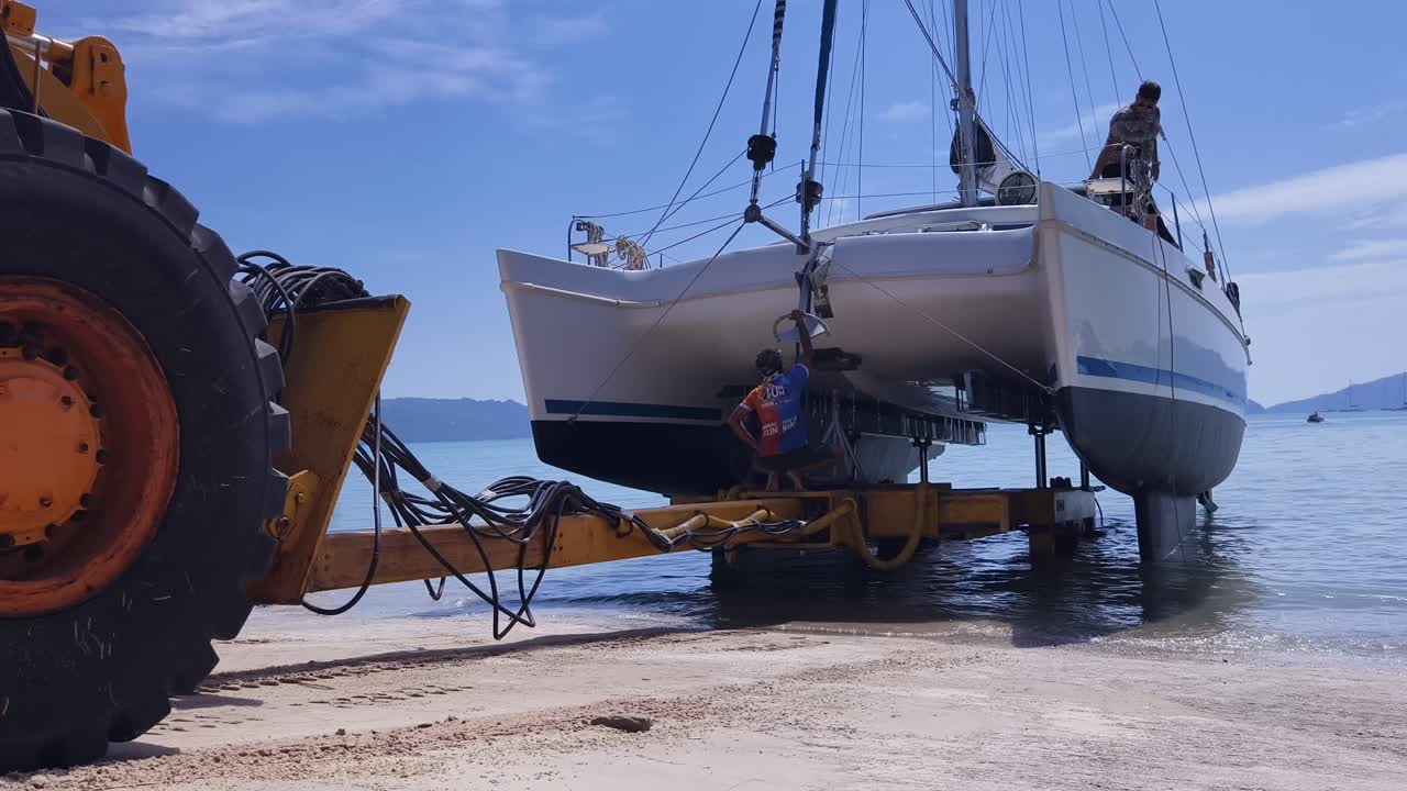 catamarán siendo transportado en un remolque por un tractor en una playa
