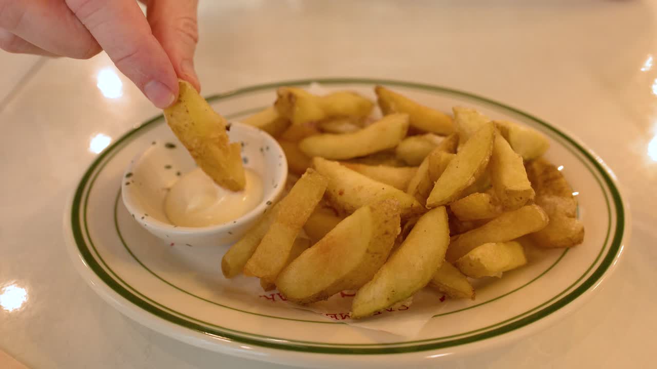 Primo piano di una mano che prende una patata a spicchio e la intinge nella salsa maionese.