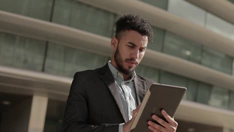 Focused middle eastern young man using tablet outdoor
