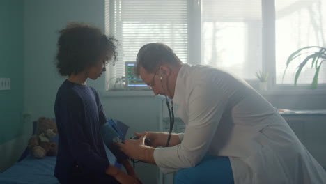 doctor measure blood pressure to african american girl in clinic office.