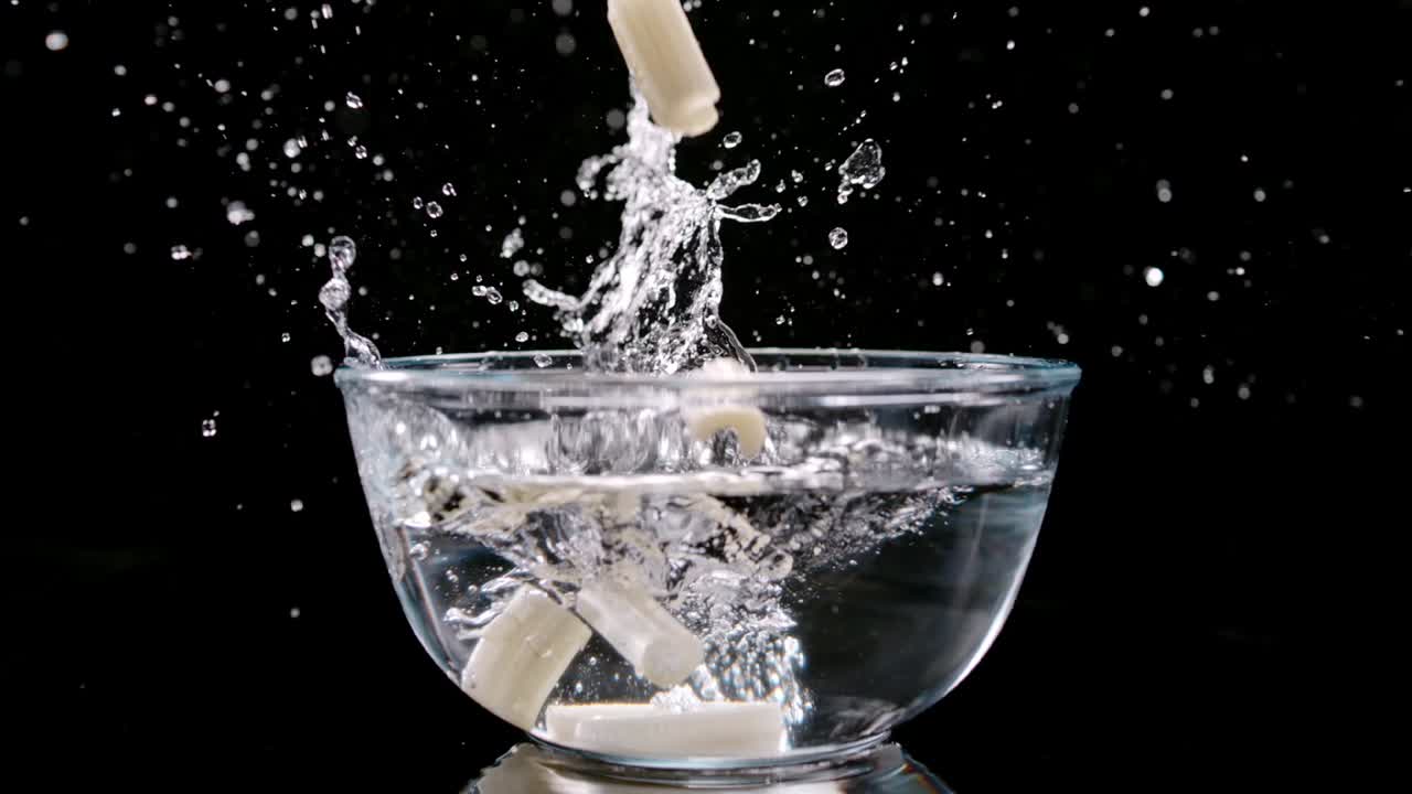Pezzi di sedano che cadono in una ciotola con acqua creando uno schizzo, al rallentatore.