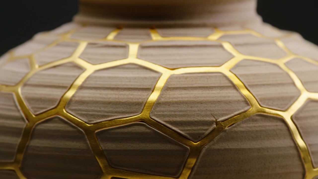 Arretrando, la telecamera rivela la parte superiore di un vaso di ceramica in studio per mostrare le giunture d'oro kintsugi.