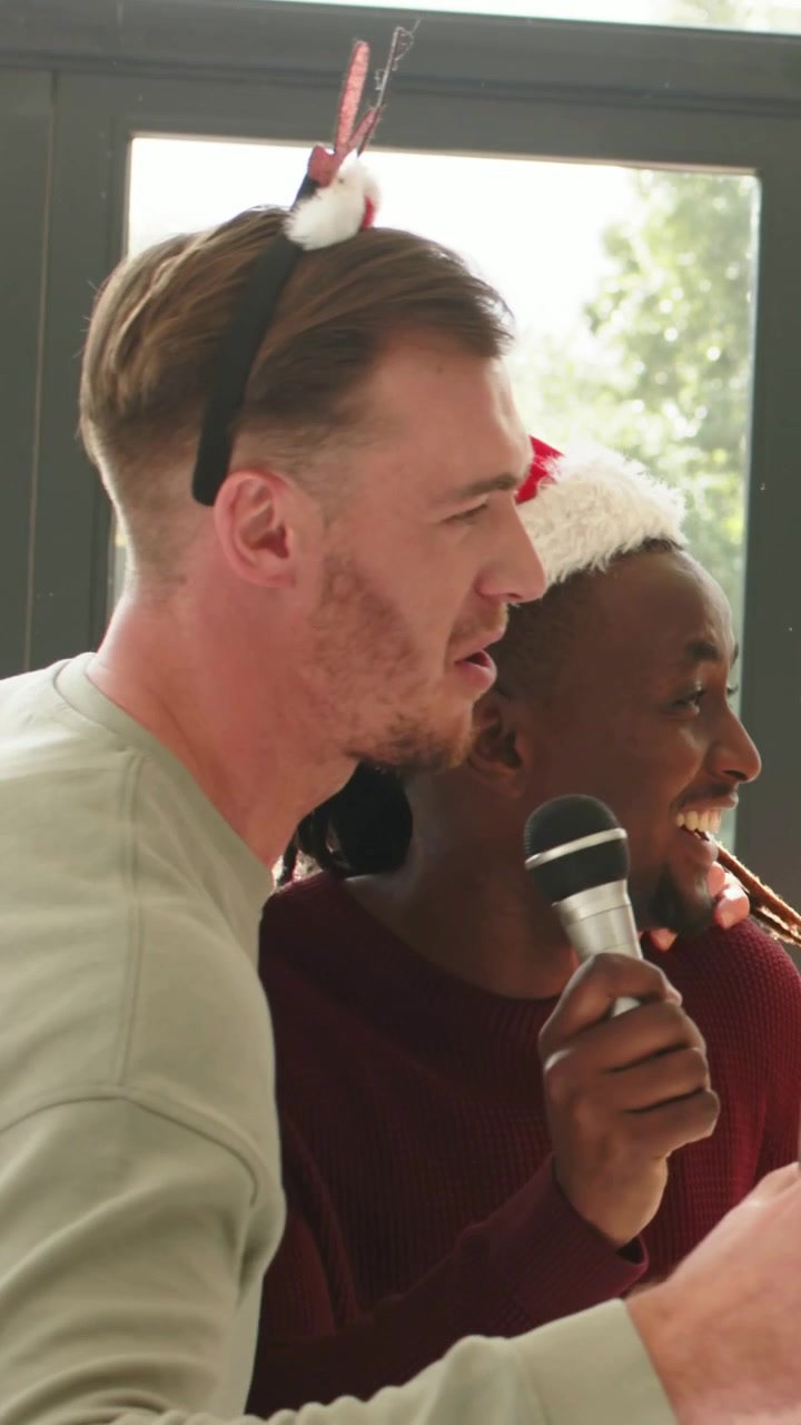 Vertical video: Raising glass, friends wearing antlers and Santa hat singing with mic at home