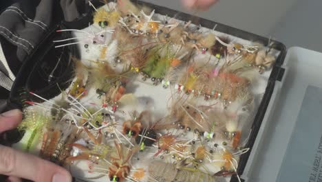 fisherman selects and showcases multicolored flies from plastic saltwater tackle box held on lap