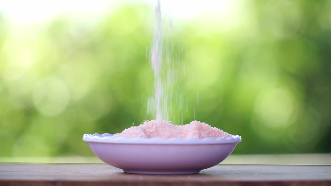 una mano humana toma una pizca de sal rosa del himalaya de un cuenco y la vierte