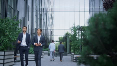 Two-successful-businessmen-walking-at-modern-office-building-discussing-project.