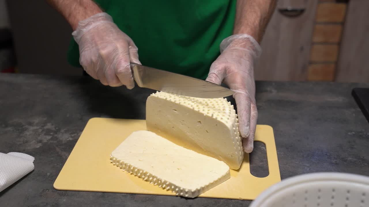 Manos con guantes cortando queso Gomolya, producto lácteo tradicional húngaro en preparación.