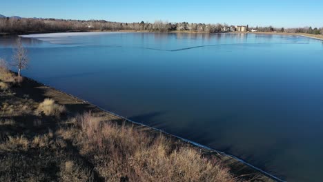 a bird-like flight over a freezing lake west of denver captures a sun soaked fall day