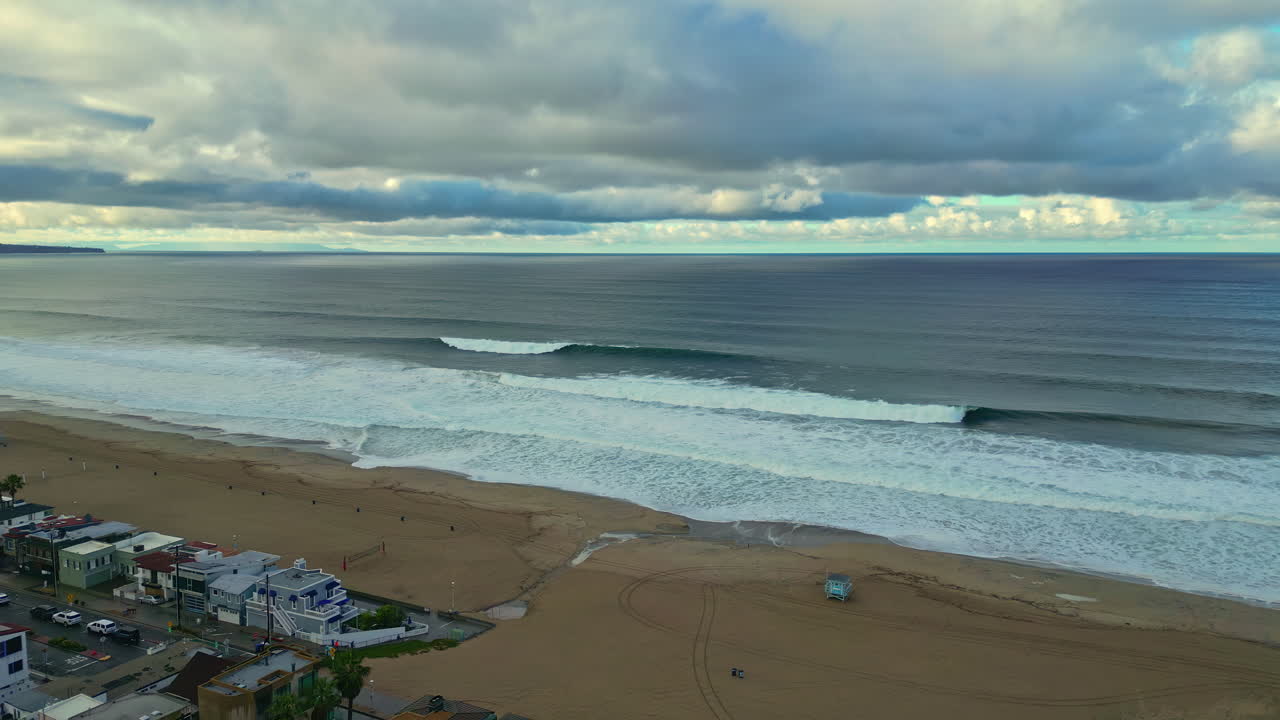 disparo aéreo de un dron volando sobre las olas que se estrellan a lo largo de la playa de manhattan con una fila de bungalows junto a la playa visibles a continuación durante la noche