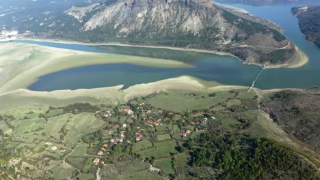 aerial pull out view of mountain and river, revealing a small village on land covered in grass and trees