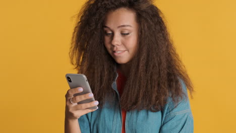 una mujer caucásica de cabello rizado usando un teléfono inteligente y riendo.