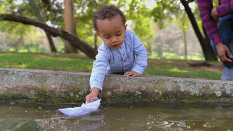 Little-boy-playing-with-paper-ship,-sailing-it-off-and-sinking