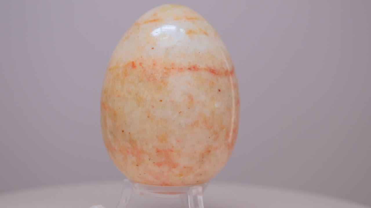 Orange and cream Marble egg rotating slowly on a turntable in front of a white background