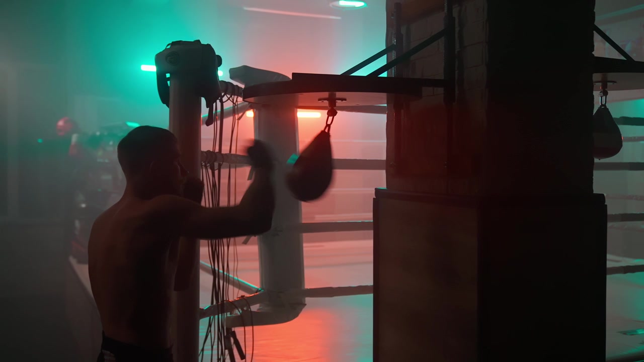 Silueta de un boxeador entrenando con una pera de velocidad en un gimnasio oscuro.