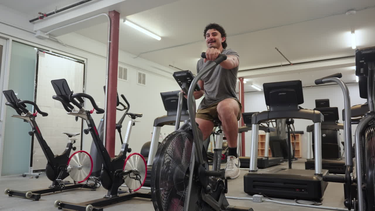 Uomo seduto che si allena su cyclette assault in palestra - Campo lungo