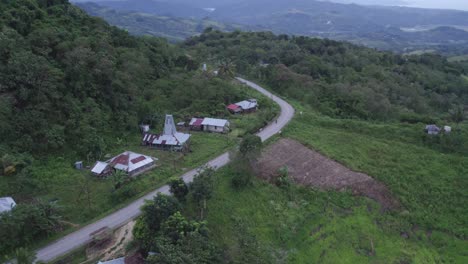 Motorbike-driving-at-road-with-small-local-houses-at-Sumba-island-Indonesia,-aerial